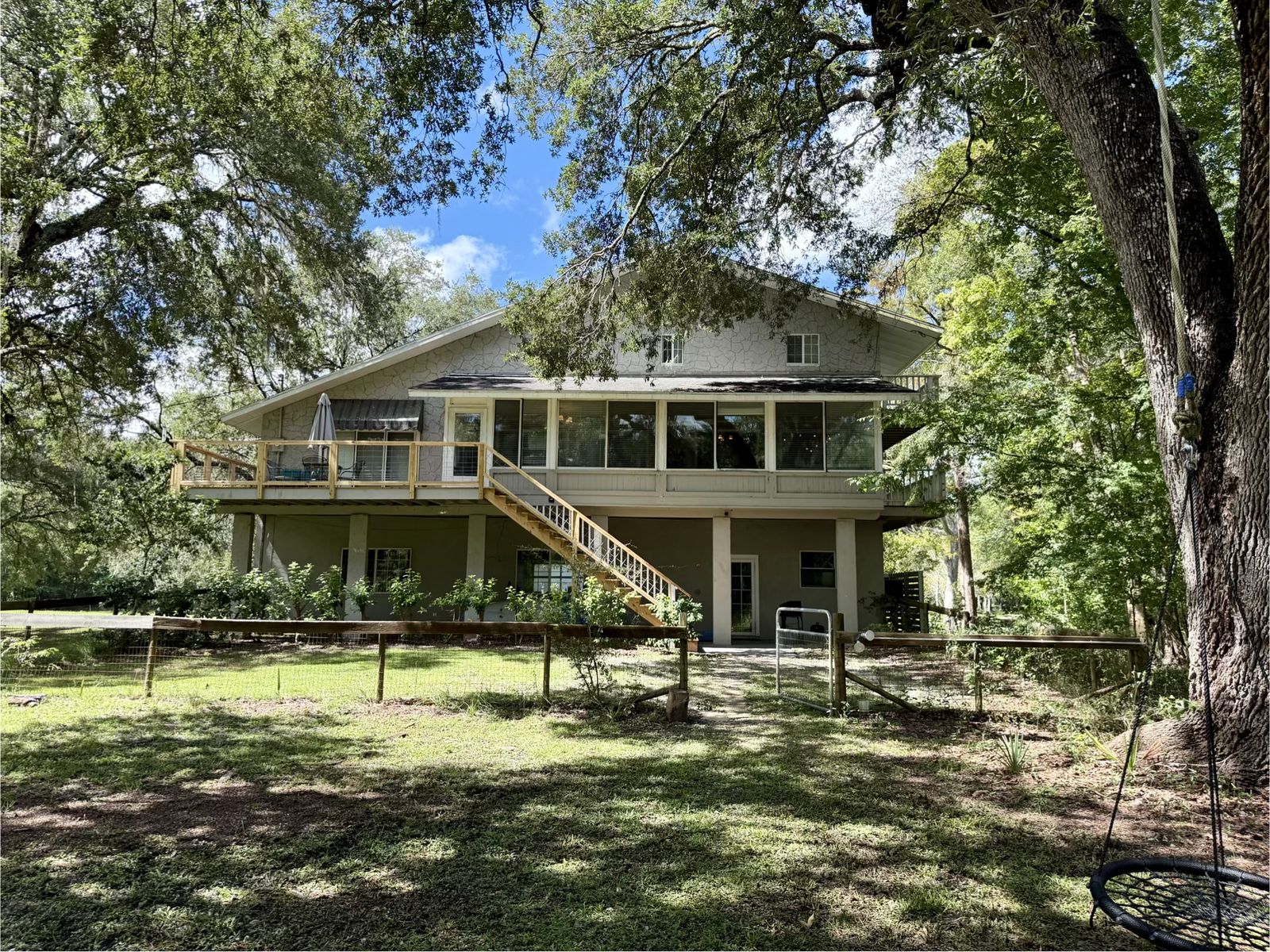 The elevated house seen from the back lawn, framed by ancient oaks