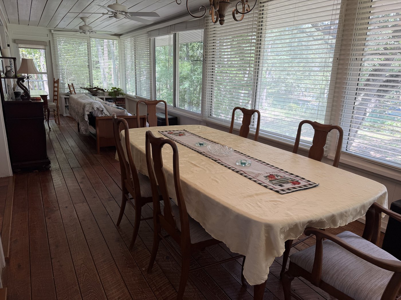 The Florida room's long dining table running beside a wall of windows into the trees